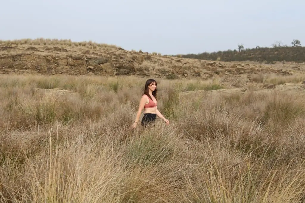 Woman walking through grassy dunes.