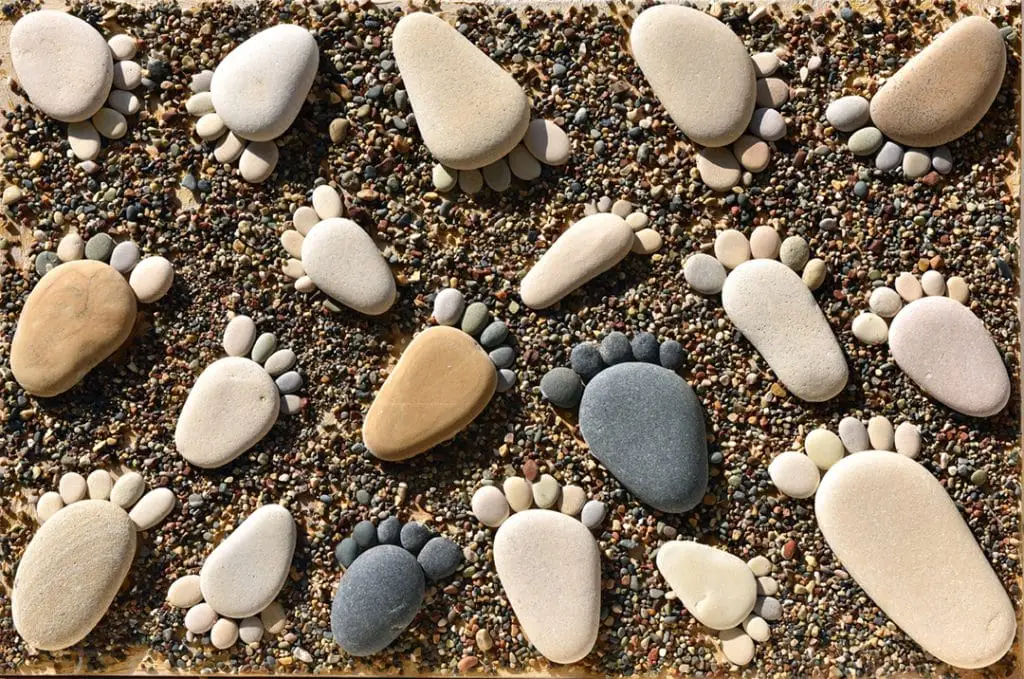 Pebbles arranged as footprints on sandy beach.