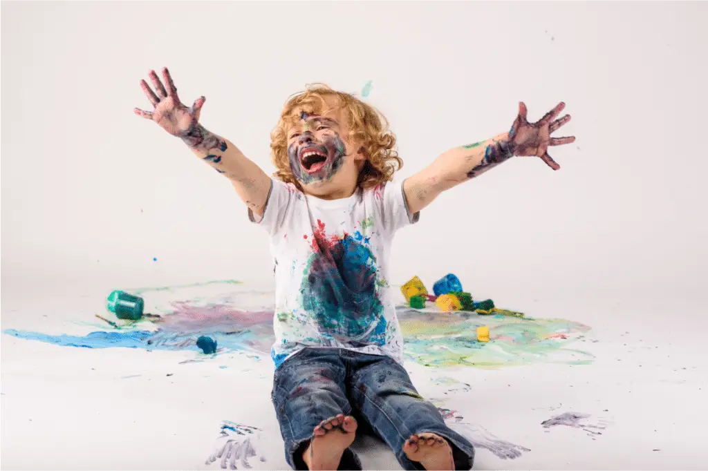 Child covered in paint, smiling with arms raised.